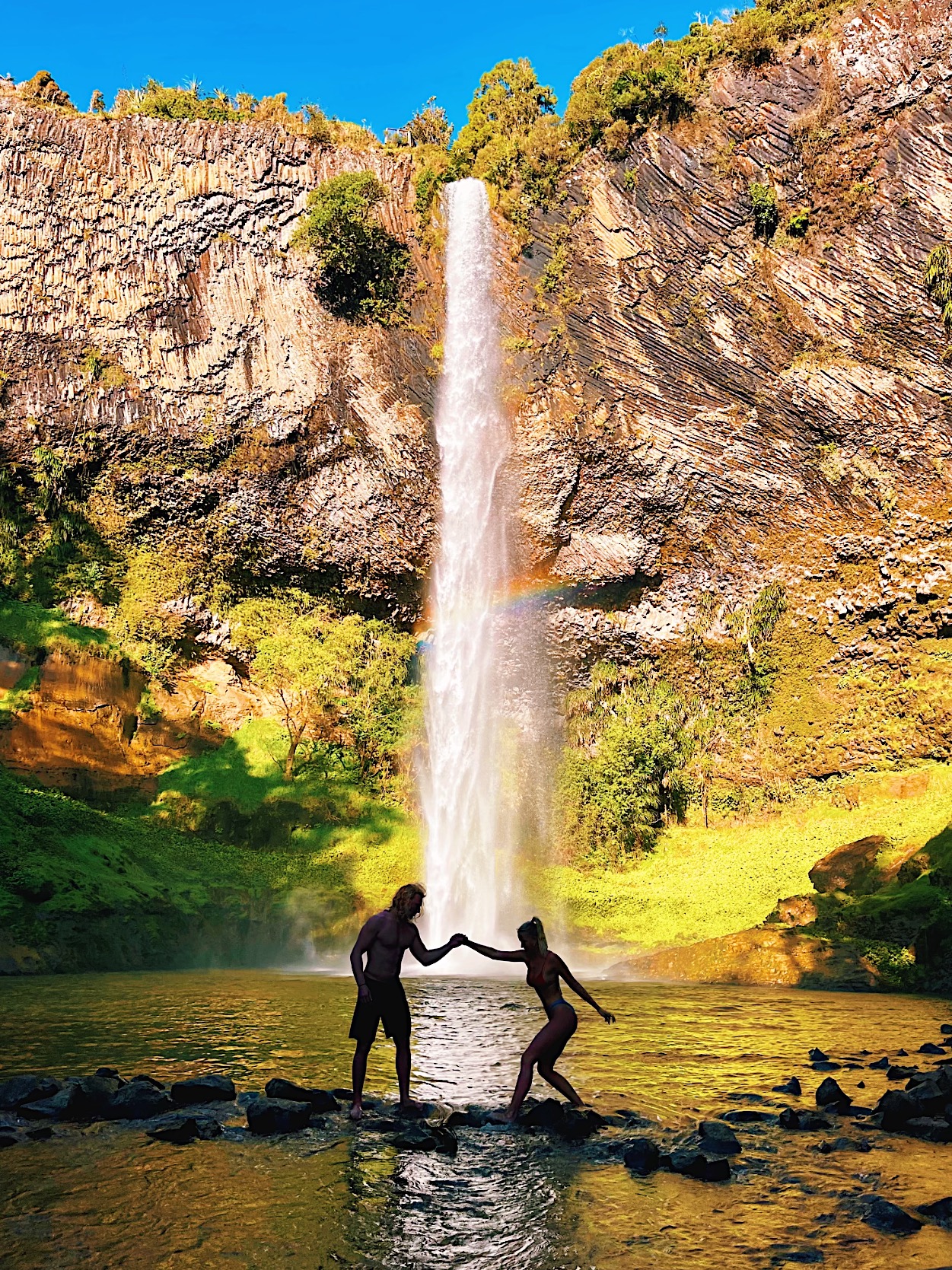 Marla and her boyfriend walking over rocks in the water in front of the waterfall